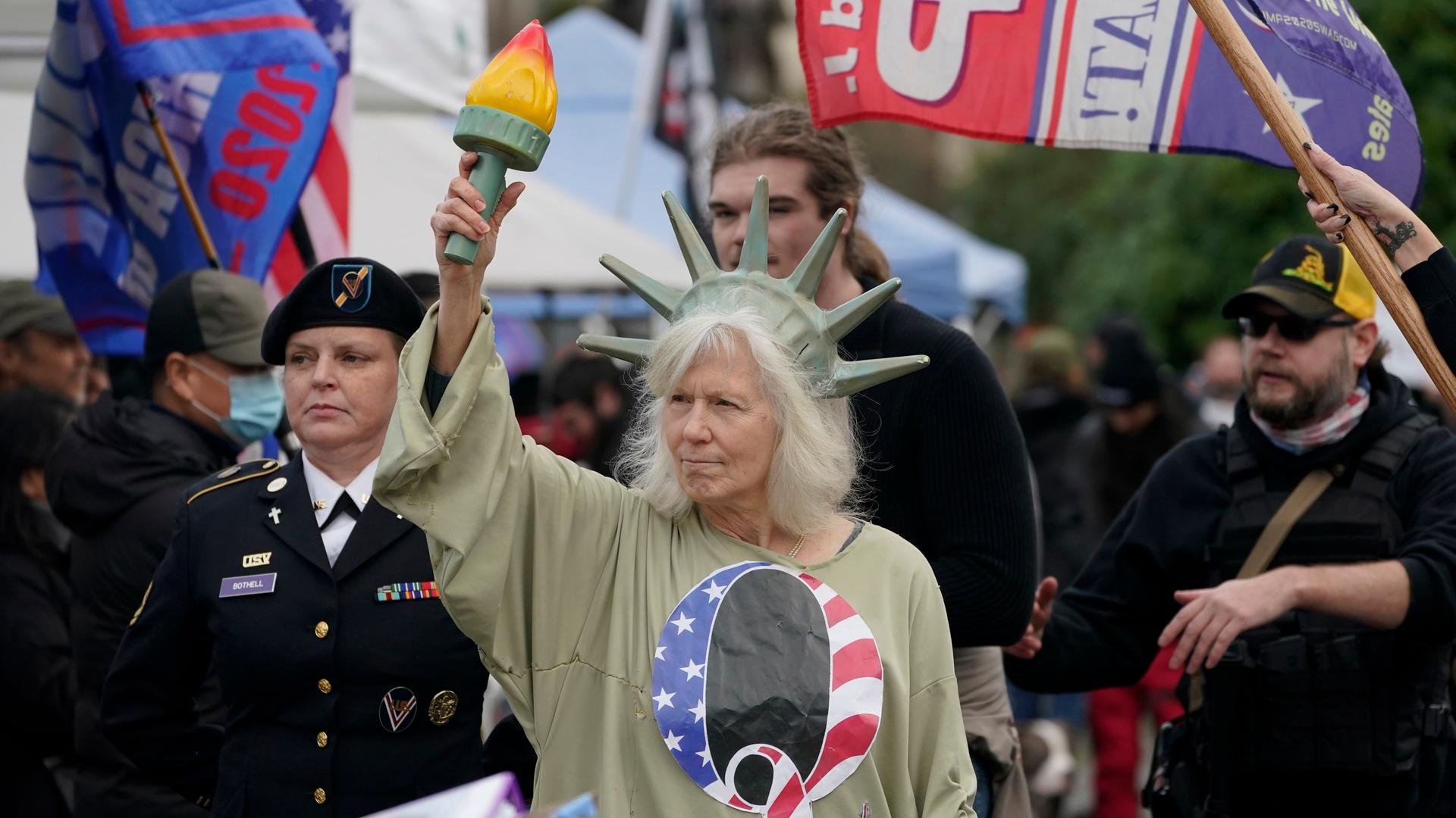 Demonstranten vor dem US-Capitol. Eine Frau hat sich als Freiheitsstatue verkleidet und trägt ein T-Shirt der rechtsextremen QAnon-Bewegung. Demonstranten vor dem US-Capitol. Eine Frau hat sich als Freiheitsstatue verkleidet und trägt ein T-Shirt der rechtsextremen QAnon-Bewegung.