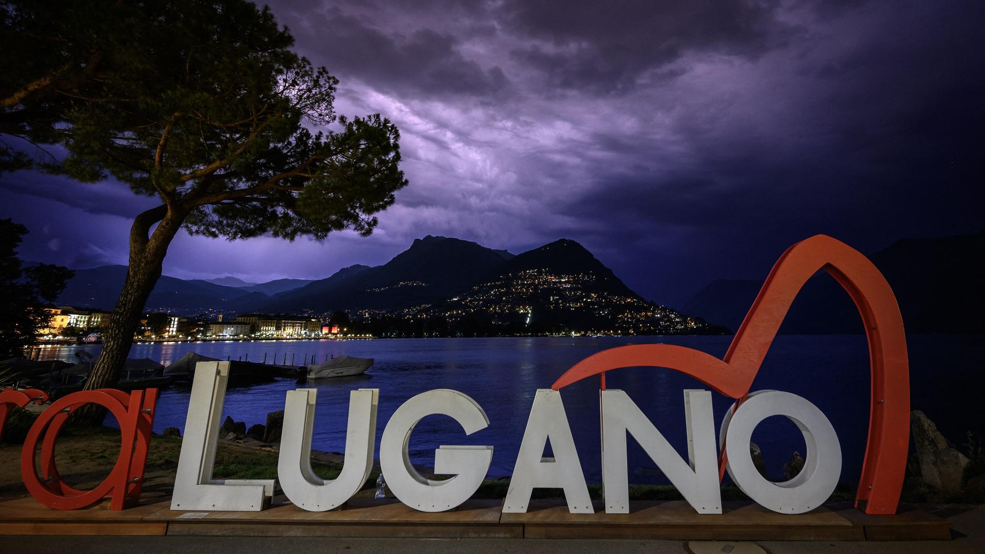 Das Logo der Konferenz in Lugano zum Wiederaufbau der kriegszerstörten Gebiete in der Ukraine vor dunklem Himmel und einem See. Das Logo der Konferenz in Lugano zum Wiederaufbau der kriegszerstörten Gebiete in der Ukraine vor dunklem Himmel und einem See.