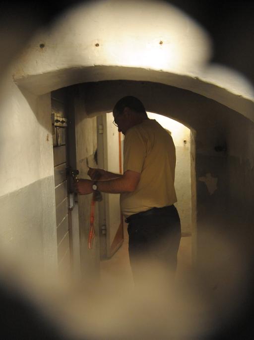 Mitarbeiter Michael Wildt von der Initiativgruppe Geschlossener Jugendwerkhof Torgau e.V. steht vor einer Zellentür im Dunkelzellentrakt des ehemaligen Jugendwerkhofes in Torgau. 
