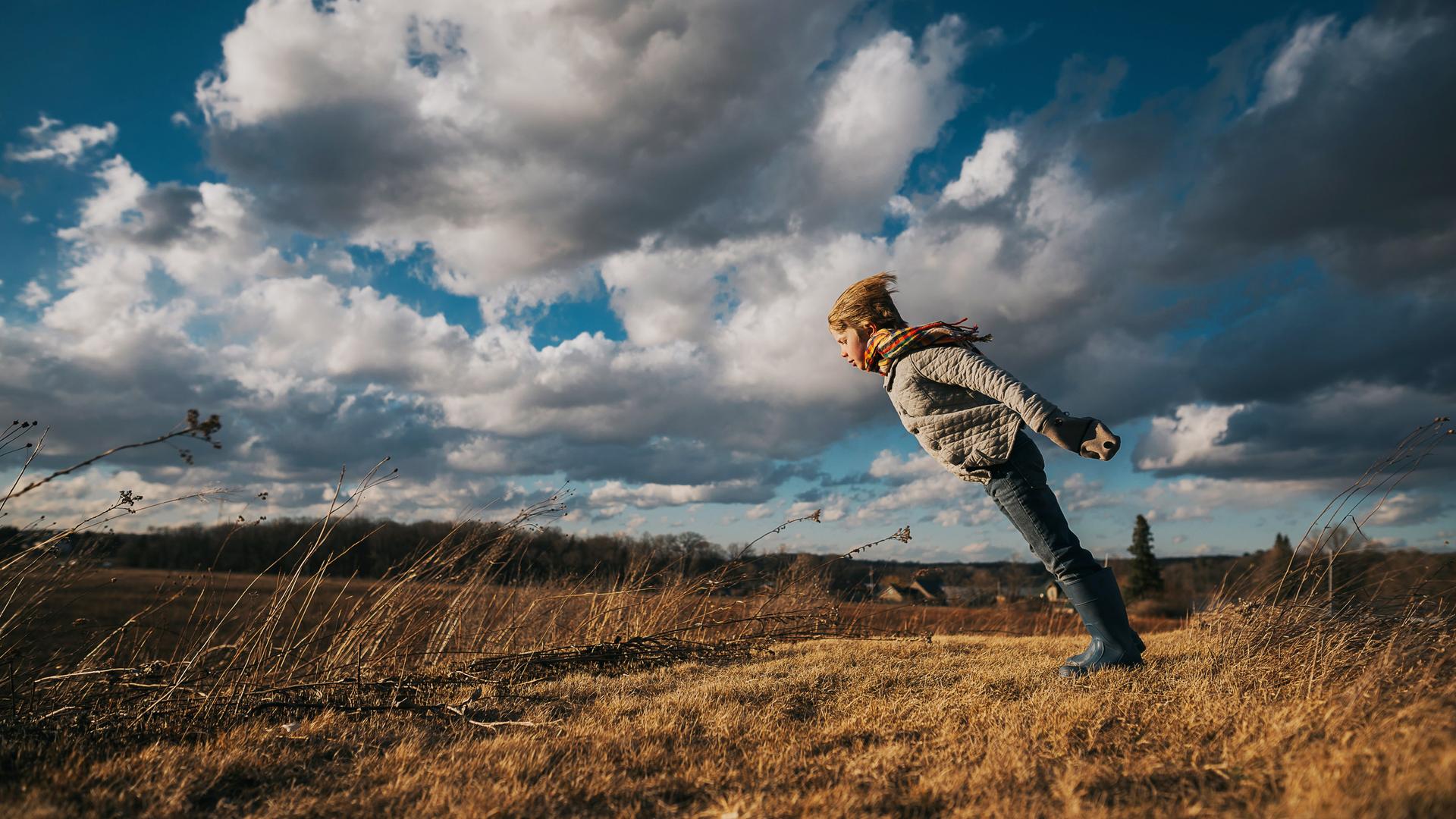 Ein Kind steht schief in den Wind gestemmt auf einem Feld.