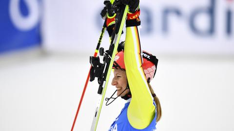 Man sieht die Skirennfahrerin Lena Dürr von der Seite. Sie hält ihre Skier hoch, trägt Helm und Skianzug und lacht.