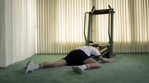Ein junger Mann hängt erschöpft am Boden vor einem Fitness Laufband.