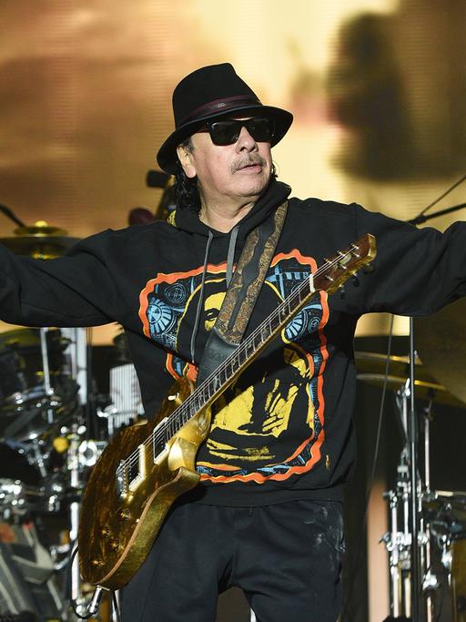 Carlos Santana steht auf einer Bühne mit Gitarre mit ausgebreiteten Armen