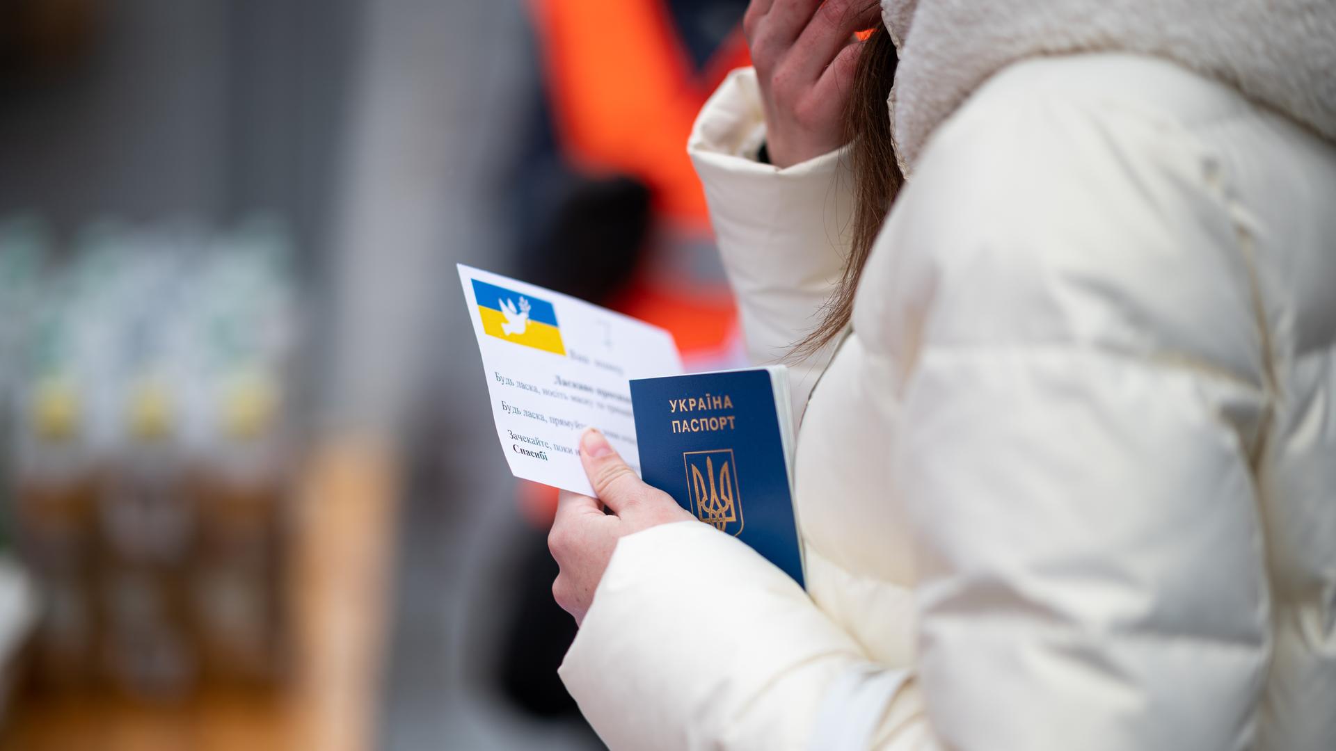 Eine junge Frau aus der Ukraine steht mit ihrem Pass in der Hand ein einer Schlange.