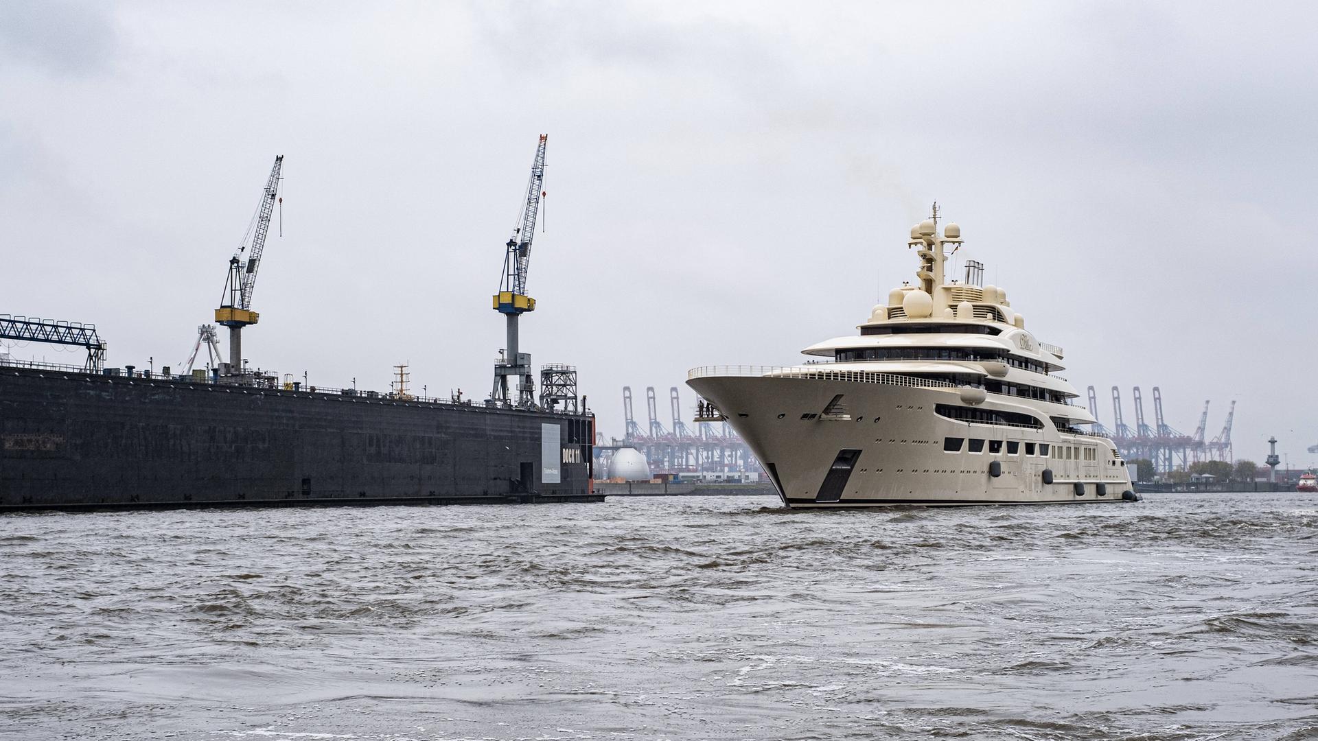 Eine weiße Yacht fährt durch den Hamburger Hafen neben Kränen. Eine weiße Yacht fährt durch den Hamburger Hafen neben Kränen.