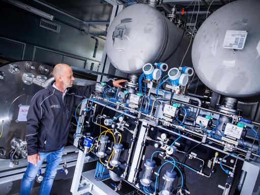 Anlagenmanager Guido König vom Unternehmen Apex Energy prüft eine Elektrolyse-Anlage, zahlreiche Rohre und Ventile sind zu sehen.