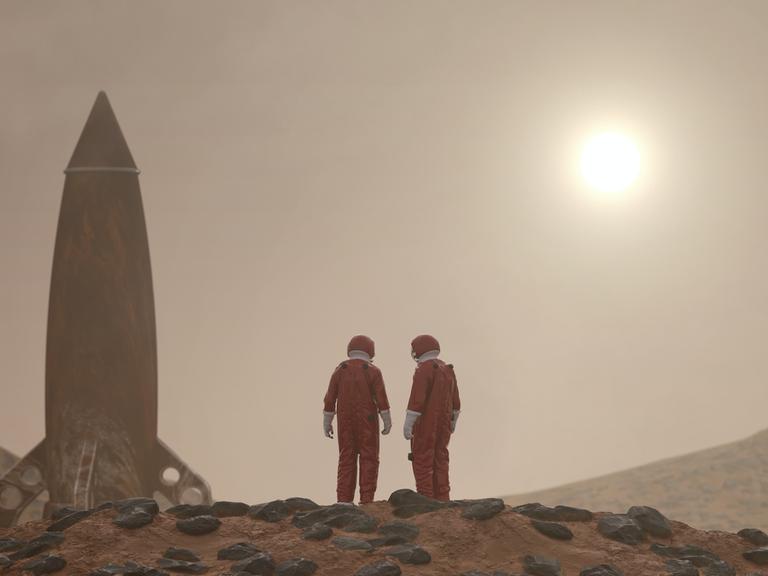 Zwei Personen in roten Ganzkörperanzügen auf rotem, steinigen Untergrund. Neben ihnen eine Rakete, aufrecht stehend. Am Horizont die Sonne.