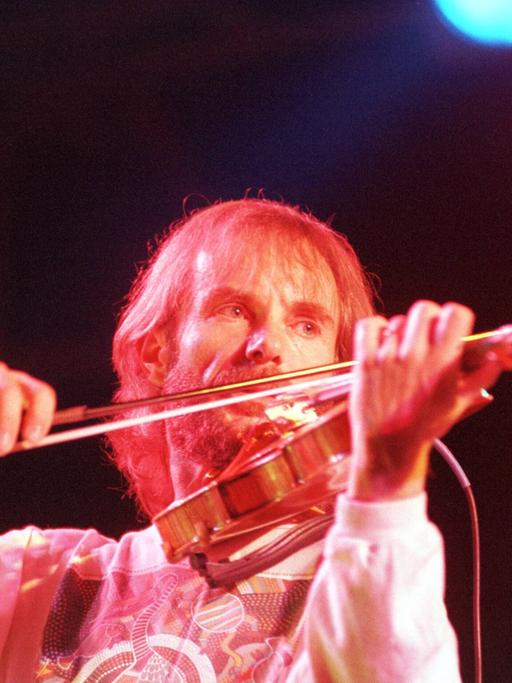 Ein bärtiger Mann spielt, angestrahlt von Bühnenlicht, Geige. 