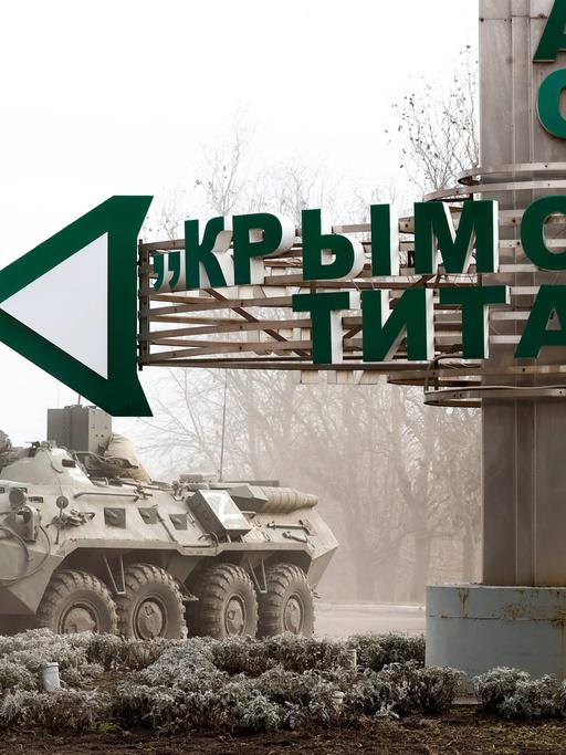 Ein Straßenschild bei dem Checkpoint Perekop an der ukrainischen Grenze weist den Weg zu der Titan-Anlage in Armyansk auf der Krim, neben dem Schild ein Panzer.