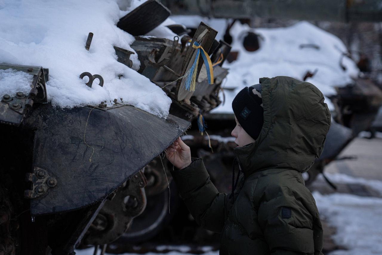 Kiew, Ukraine: Ein Junge steht im Winter neben einem zerstörten Fahrzeug der russischen Armee. 
