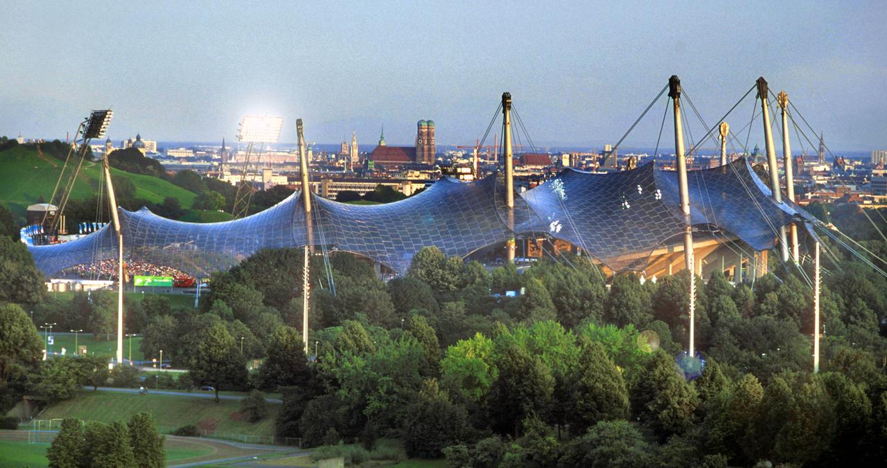 Das Olympiagelände in München mit dem Zeltdach des Stadions, entworfen vom Bürö Behnisch & Partner für die olympischen Spiele 1972. Im Hintergrund das Stadtpanorama mit Frauenkirche