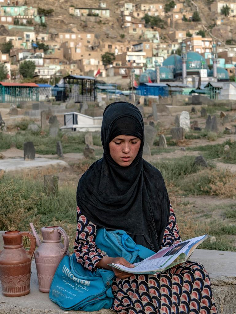 Eine 14-jährige Wasserverkäuferin auf einem Kabuler Friedhof, lesend, während sie auf Kundschaft wartet