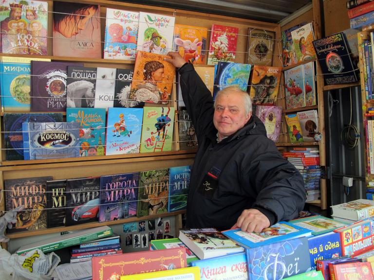 Ein älterer Mann steht in seinem Bücherstand und zeigt eines seiner Kinderbücher.