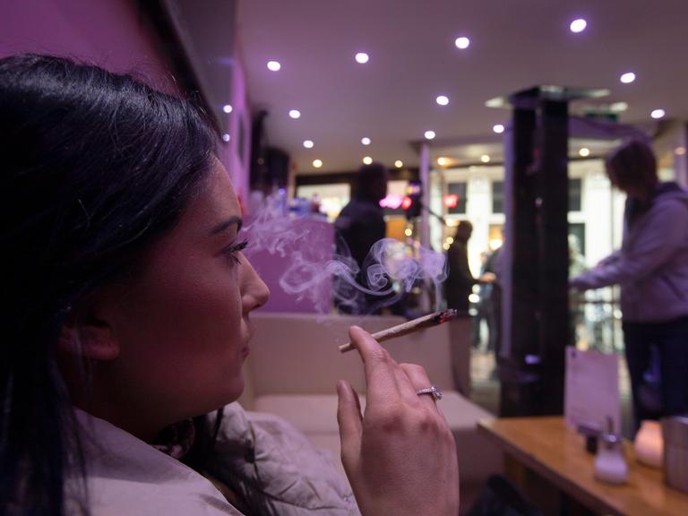 Eine Frau sitz in Amsterdam in einem Coffeeshop und raucht einen Joint.