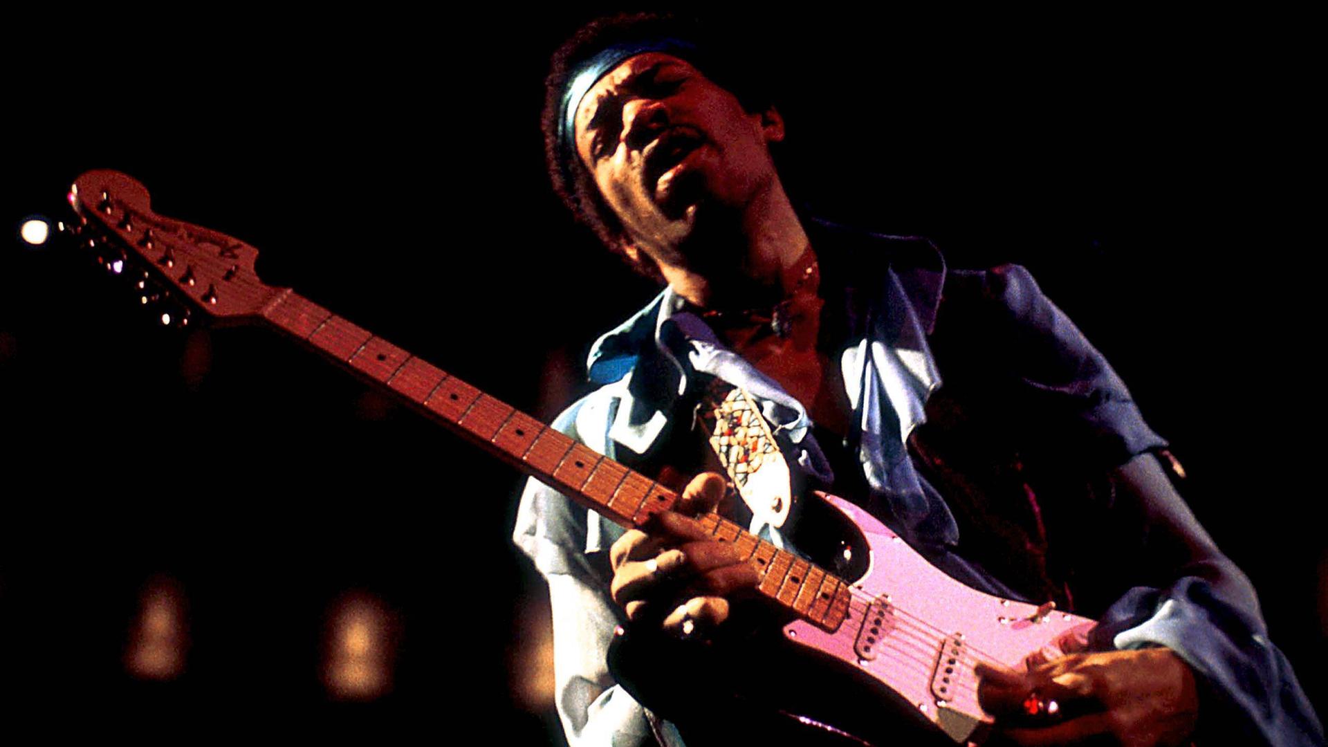 Jimi Hendrix steht mit seiner E-Gitarre auf einer Bühne Jimi Hendrix steht mit seiner E-Gitarre auf einer Bühne