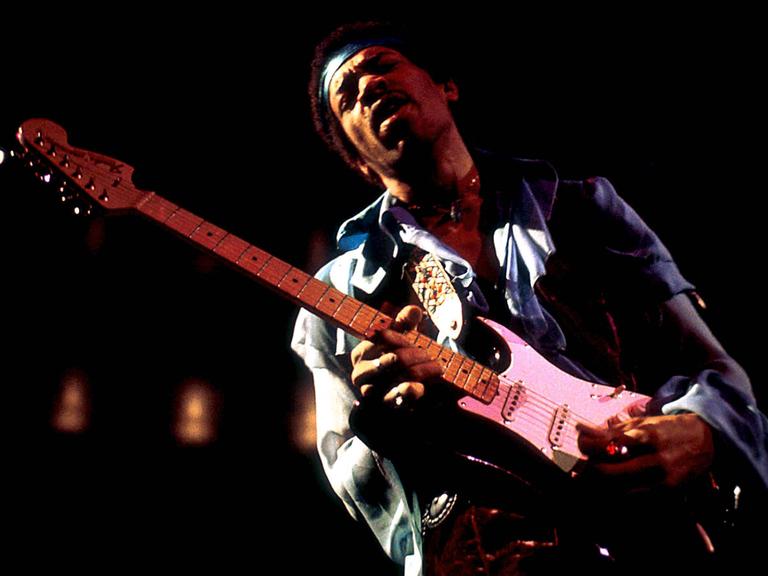 Jimi Hendrix steht mit seiner E-Gitarre auf einer Bühne