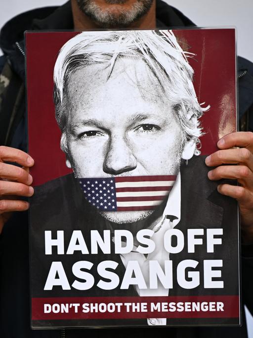 Ein Aktivist hält ein Plakat von WikiLeaks Gründer Julian Assange, der den Mund mit einer amerikanischen Flagge zugeklebt hat. Der Text darauf lautet: "Hands off Assange. Don't shoot the Messenger", London, April 2022.