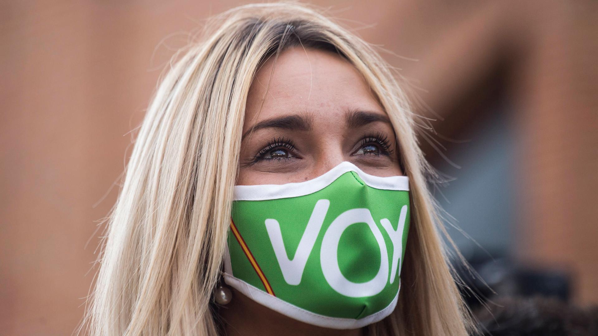 Eine junge blonde Frau trägt eine grüne Maske, auf der mit weißen Buchstaben Vox steht. Eine junge blonde Frau trägt eine grüne Maske, auf der mit weißen Buchstaben Vox steht.