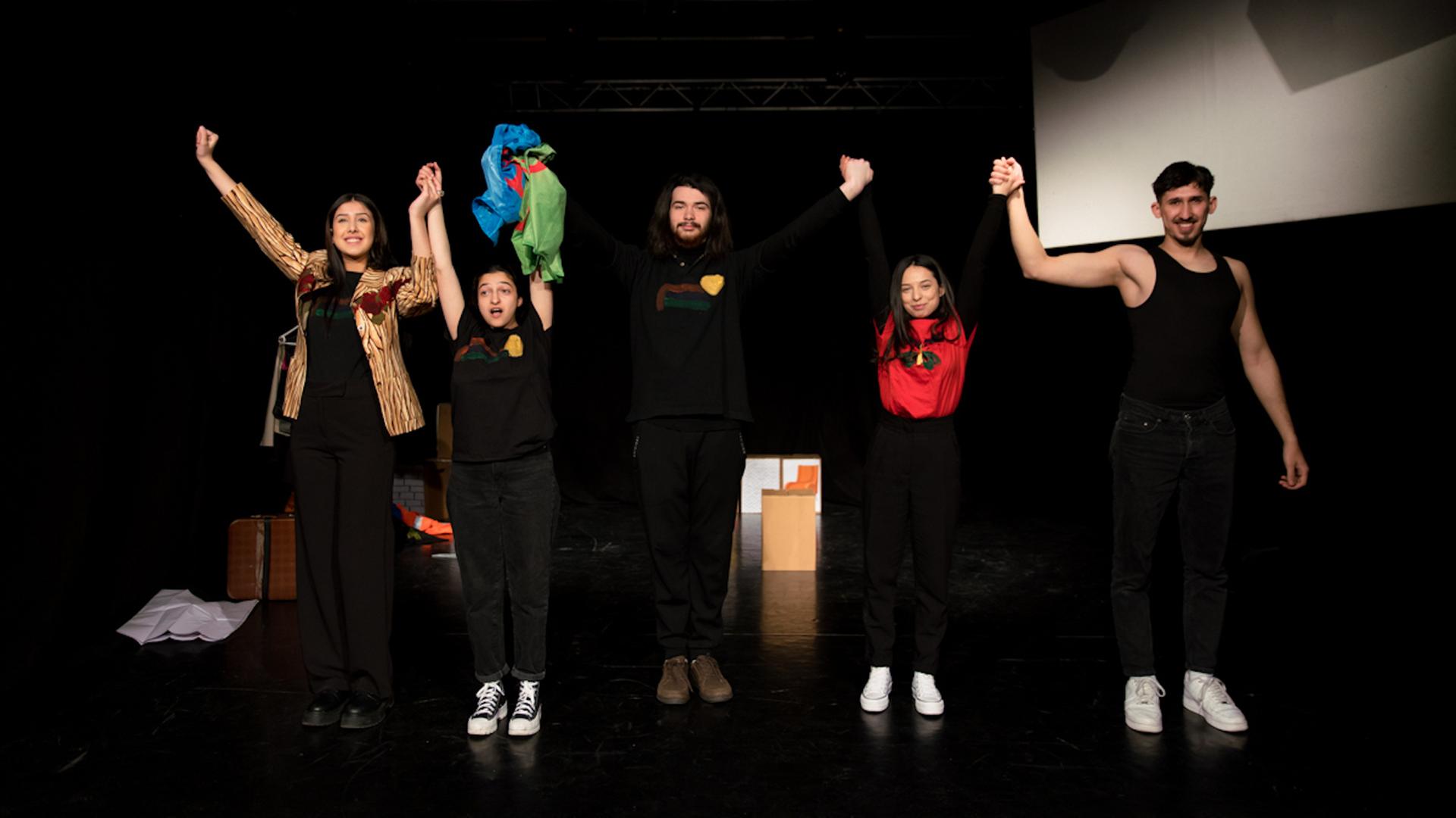 Fünf junge Mitglieder der Theatergruppe stehen mit erhobenen Armen jubelnd auf der Bühne. Fünf junge Mitglieder der Theatergruppe stehen mit erhobenen Armen jubelnd auf der Bühne.