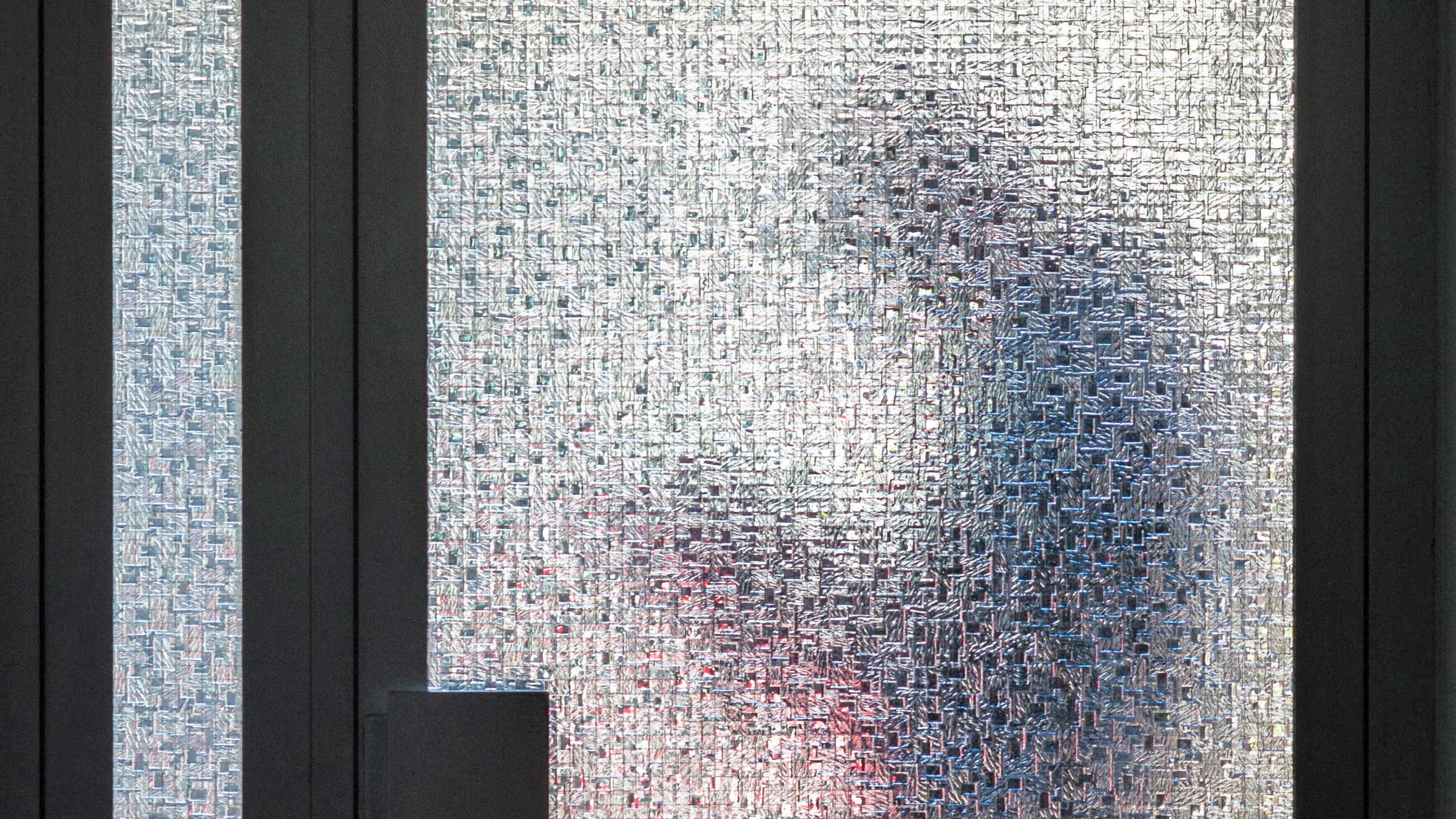 Silhouette eines Mannes mit Smartphone in den Händen, aufgenommen durch ein strukturierte Glastür eines Hauses.