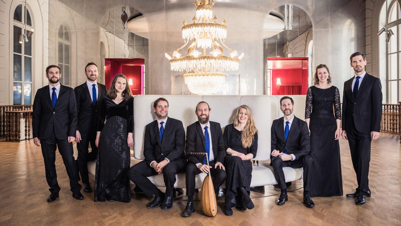 Das Ensemble Voces Suaves sitzt zum Teil mit Instrumenten in einem historischen Raum mit ausladender Couch und dominanten Kronleuchter.