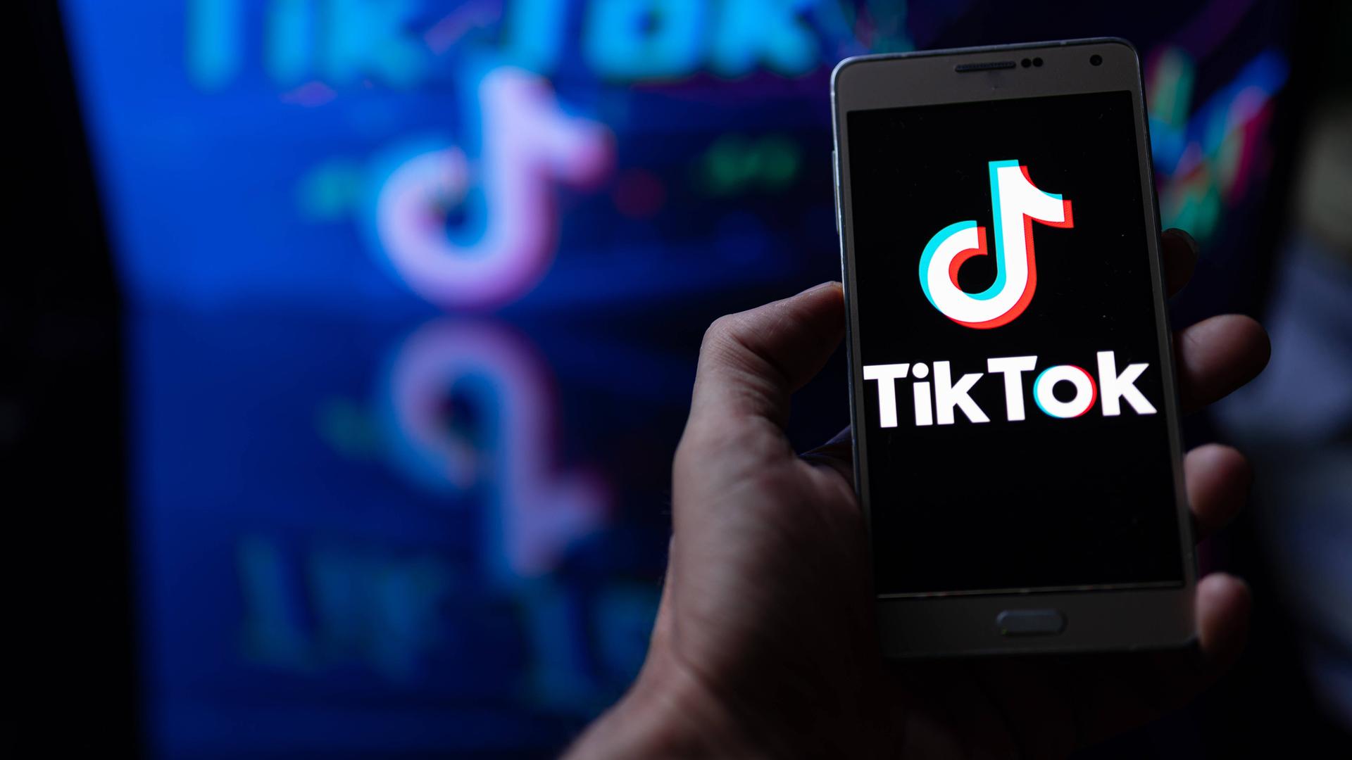 Auf dem Bild ist ein Handy zu sehen. Auf dem Display leuchtet das TikTok Logo auf. Auf dem Bild ist ein Handy zu sehen. Auf dem Display leuchtet das TikTok Logo auf.