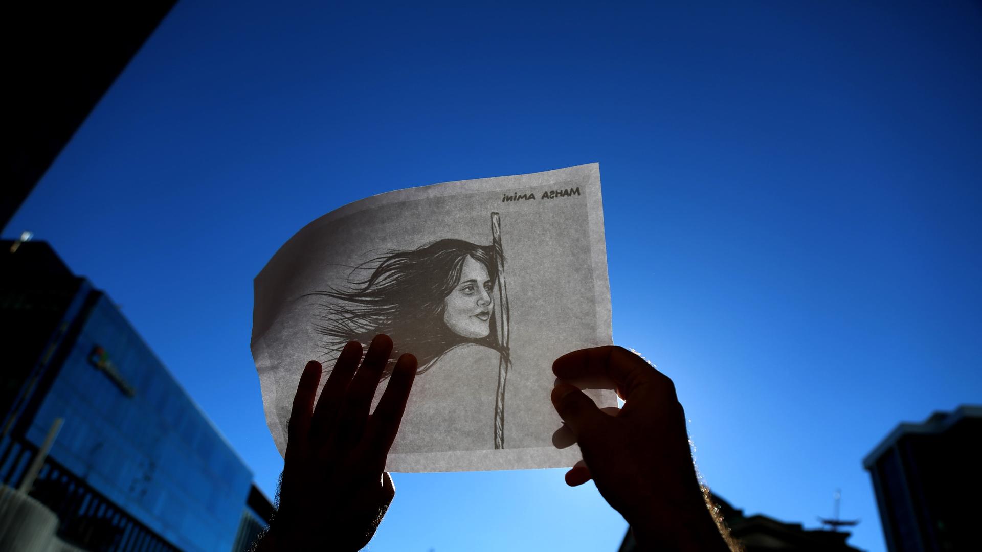 Zeichnung von Mahsa Amini, deren Haare eine Flagge bilden, auf einem Plakat, das während eines Protests hochgehalten wird. Zeichnung von Mahsa Amini, deren Haare eine Flagge bilden, auf einem Plakat, das während eines Protests hochgehalten wird.