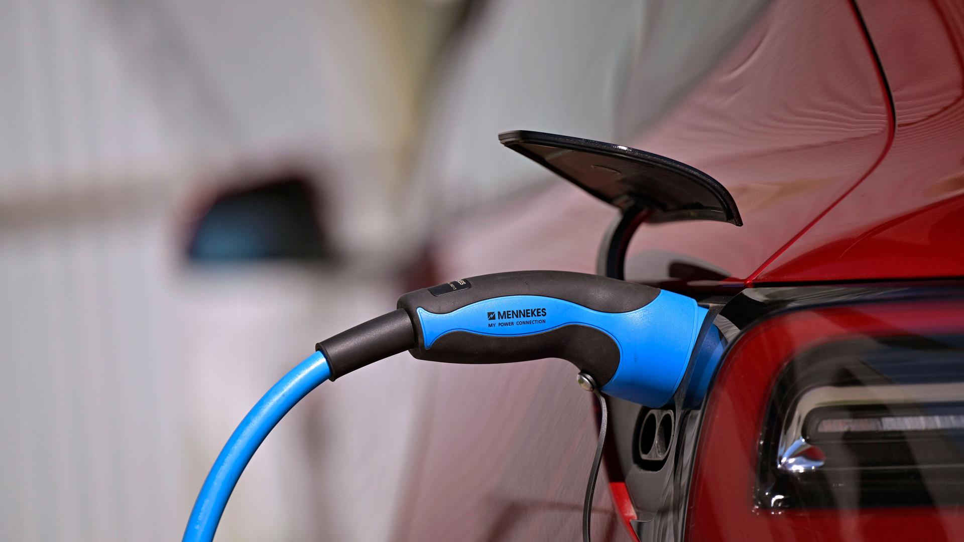 Öffentliche Ladesäule für E-Autos an einem Parkplatz. Ein Tesla Model 3 lädt gerade seinen Akku an der Stromtankstelle voll, der Stecker steckt im Ladeanschluss des Autos. Öffentliche Ladesäule für E-Autos an einem Parkplatz. Ein Tesla Model 3 lädt gerade seinen Akku an der Stromtankstelle voll, der Stecker steckt im Ladeanschluss des Autos.