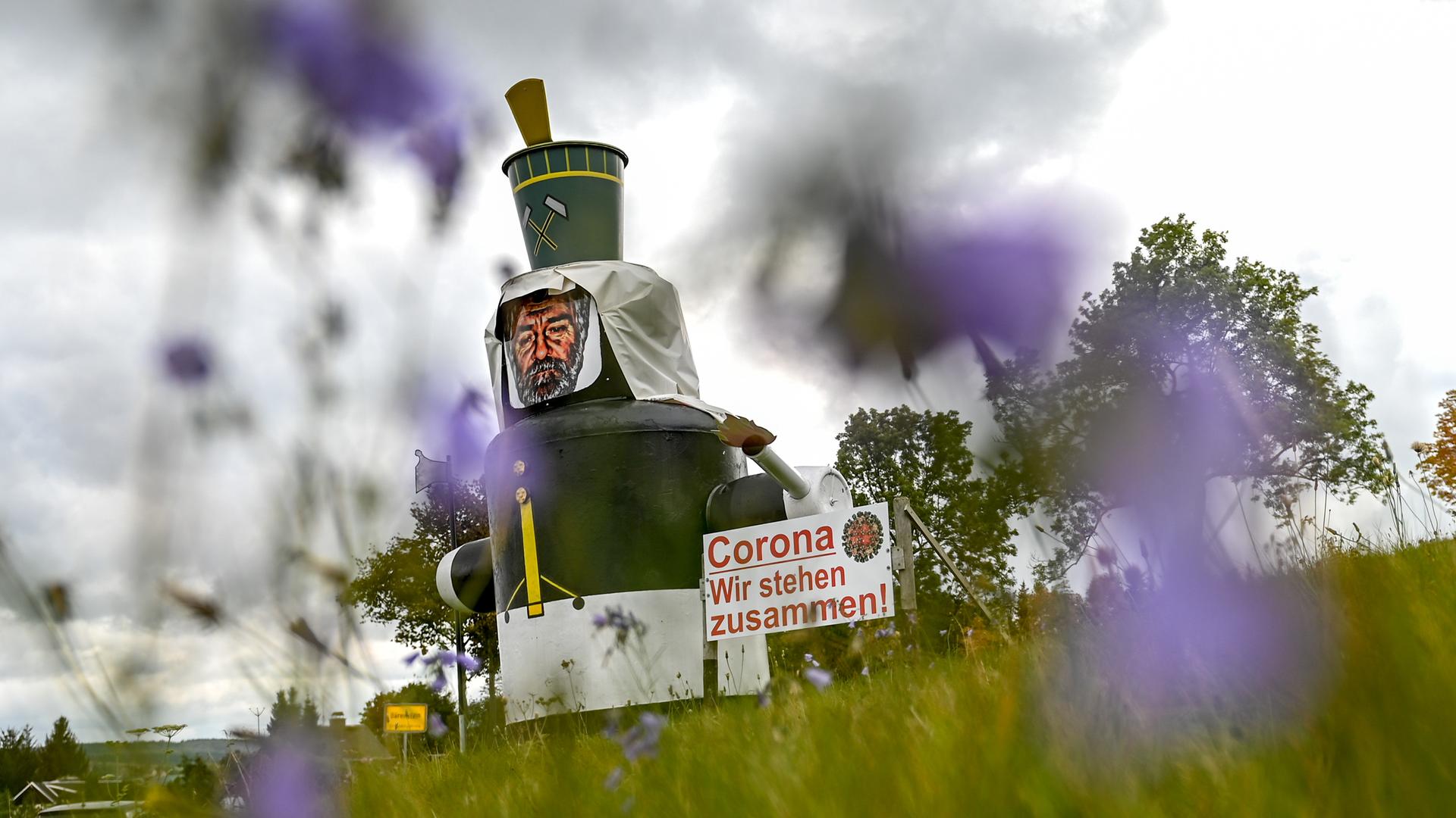 Auf einer Wiese am Ortseingang von Annaberg-Buchholz steht neben einer stilisierten Figur eines Bergmannes ein Schild mit der Aufschrift "Corona. Wir stehen zusammen!". Auf einer Wiese am Ortseingang von Annaberg-Buchholz steht neben einer stilisierten Figur eines Bergmannes ein Schild mit der Aufschrift "Corona. Wir stehen zusammen!".