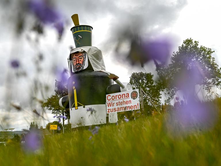 Auf einer Wiese am Ortseingang von Annaberg-Buchholz steht neben einer stilisierten Figur eines Bergmannes ein Schild mit der Aufschrift "Corona. Wir stehen zusammen!". 