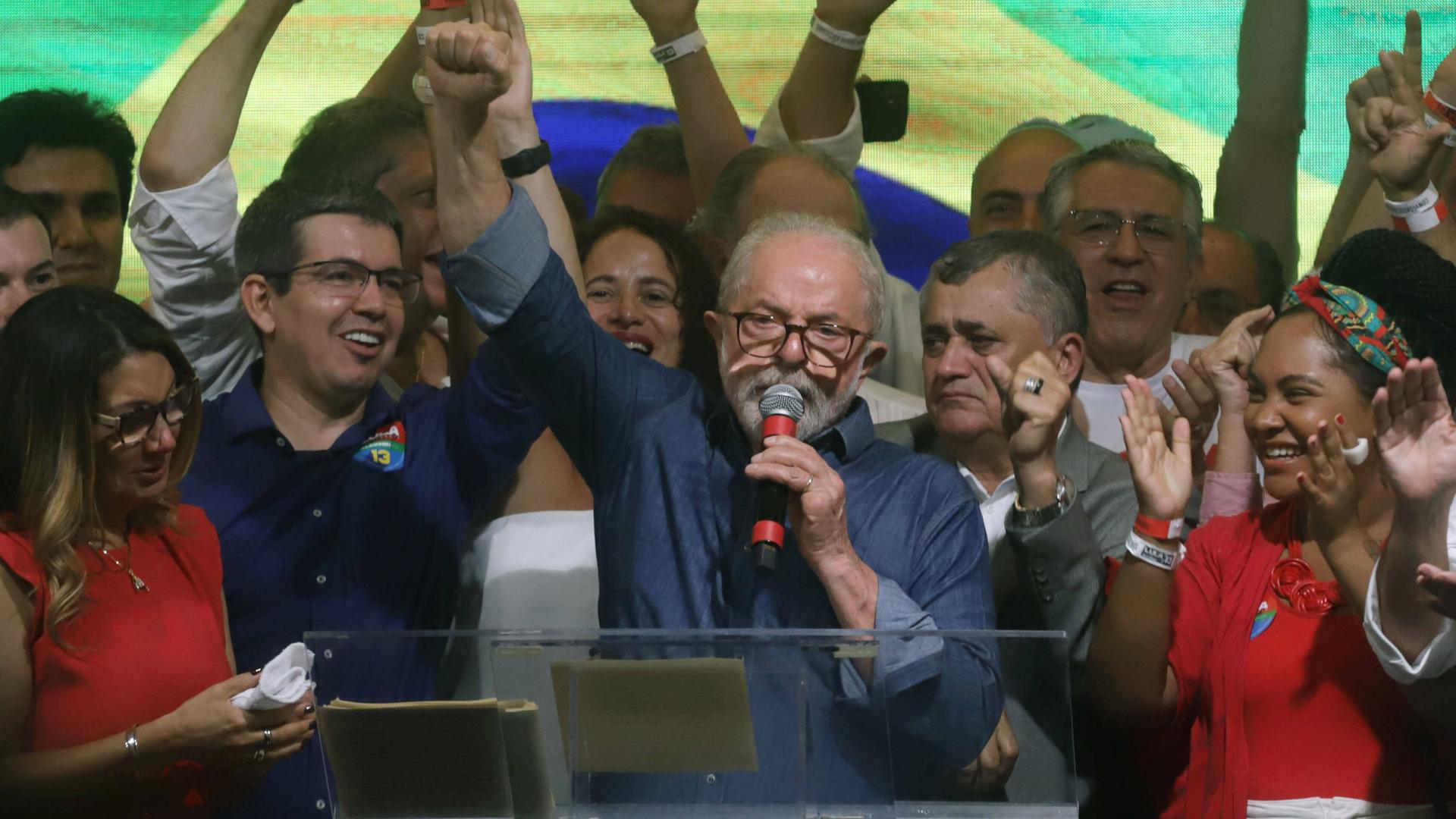 Lula da Silva steht inmitten jubelnder Anhänger, spricht in ein Mikrofon und hebt die rechte Faust. Lula da Silva steht inmitten jubelnder Anhänger, spricht in ein Mikrofon und hebt die rechte Faust.