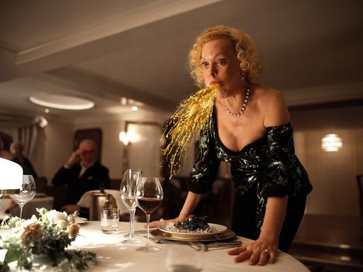 Der Film "Triangle of Sadness", bei den Oscars 2023 nominiert: Eine Frau speiht eine Art Goldregen an einem festlichen gedeckten Tisch.