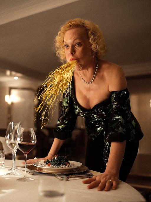 Der Film "Triangle of Sadness", bei den Oscars 2023 nominiert: Eine Frau speiht eine Art Goldregen an einem festlichen gedeckten Tisch.