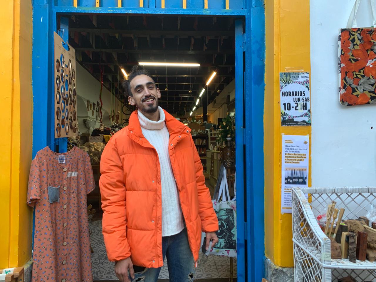 Ein hochgewachsener schlanker Jugendlicher in knallorangenem dicken Anorak steht an der offenen Tür eines Ladens mit Klamotten und Möbeln. Ein hochgewachsener schlanker Jugendlicher in knallorangenem dicken Anorak steht an der offenen Tür eines Ladens mit Klamotten und Möbeln.