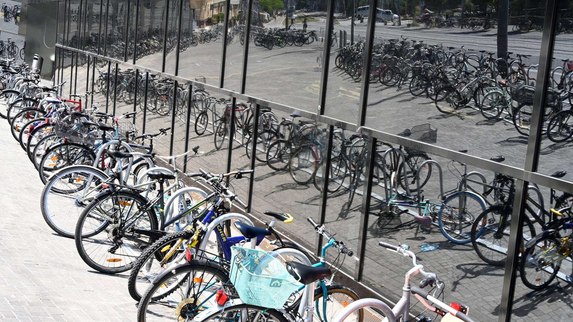 Viele abgestellte Fahrräder vor der Universitätsbibliothek in Freiburg, die sich in der Fassade spiegeln.