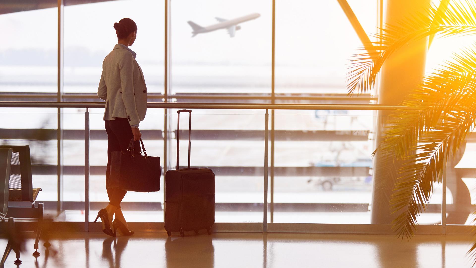 Eine Geschäftsfrau am Flughafen schaut beim Warten auf ein abhebendes Flugzeug.