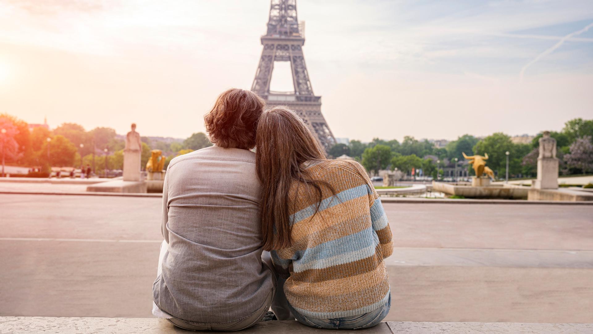 Ein Mann und eine Frau reiferen Alters sitzen eng aneinandergeschmiegt und betrachten den Eiffelturm in Paris. Sie sind in Rückenansicht zu sehen. Ein Mann und eine Frau reiferen Alters sitzen eng aneinandergeschmiegt und betrachten den Eiffelturm in Paris. Sie sind in Rückenansicht zu sehen.