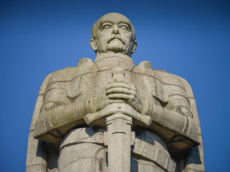 Otto von Bismarck blickt gerade aus und hält ein Schwert in den Händen.