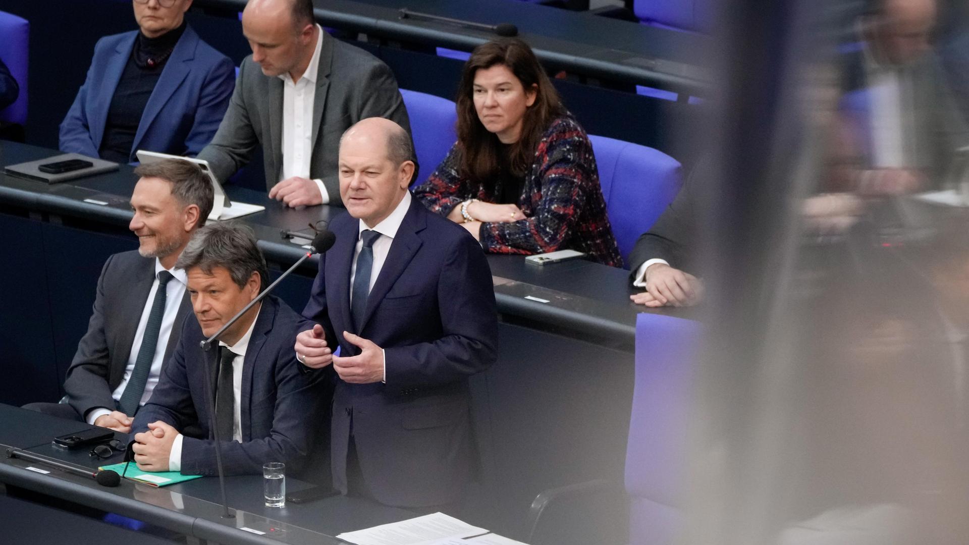 Bundeskanzler Olaf Scholz (SPD, rechts) gemeinsam mit Wirtschafts- und Klimaminister Robert Habeck (Grüne) und Finanzminister Christian Lindner (FDP) auf der Regierungsbank bei der Befragung des Bundeskanzlers. Alle drei tragen dunkle Anzüge, Scholz steht, die beiden Minister sitzen.