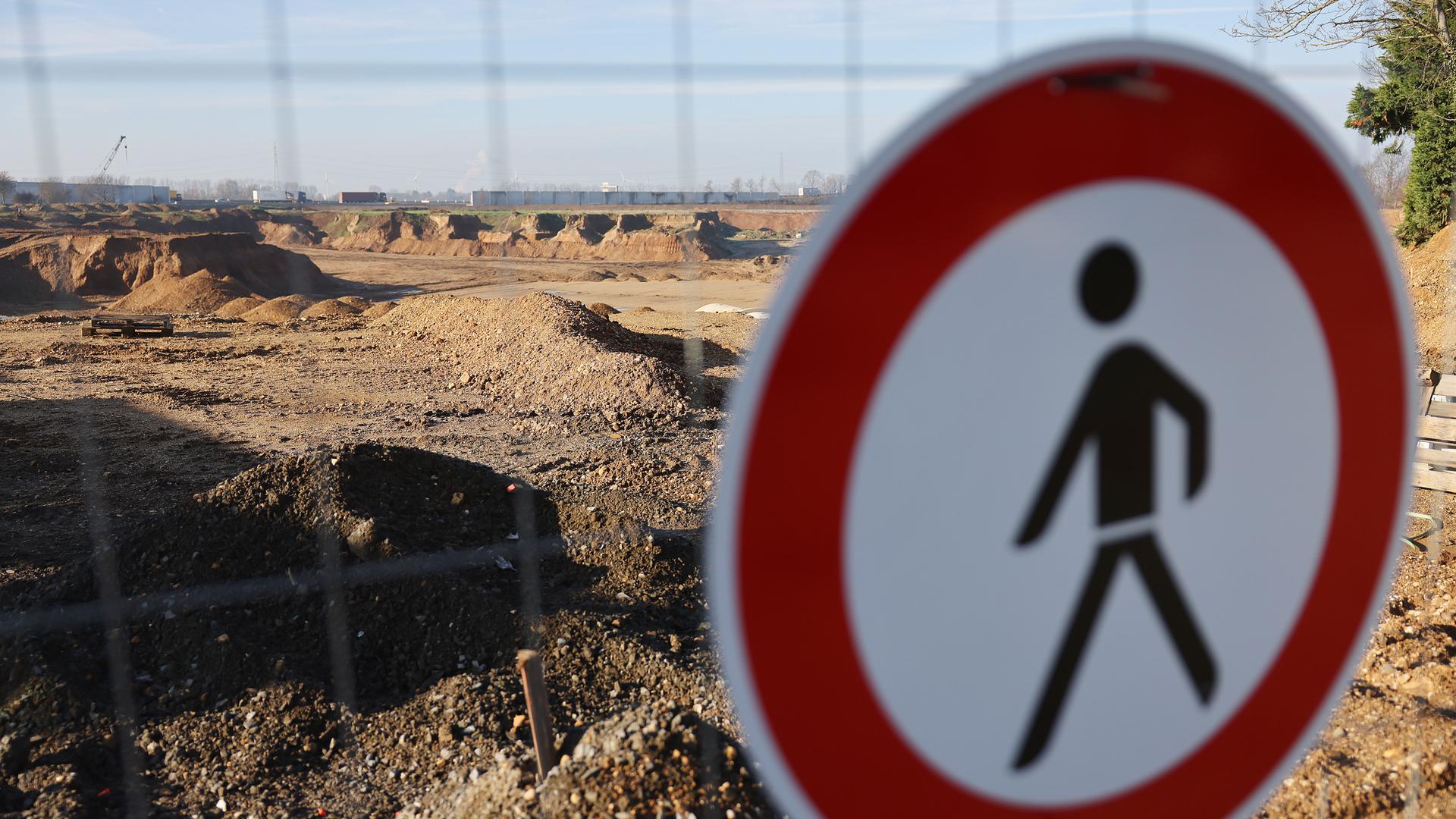Das Verkehrsschild "Verbot für Fußgänger" hängt an einem Bauzaum, hinter dem eine gigantische Sandlandschaft zu sehen ist. Das Verkehrsschild "Verbot für Fußgänger" hängt an einem Bauzaum, hinter dem eine gigantische Sandlandschaft zu sehen ist.