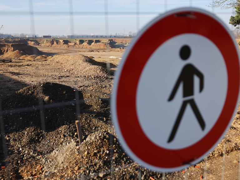 Das Verkehrsschild "Verbot für Fußgänger" hängt an einem Bauzaum, hinter dem eine gigantische Sandlandschaft zu sehen ist.