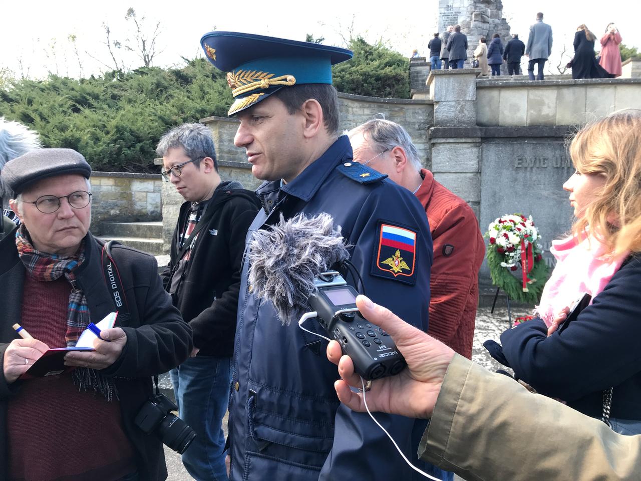 Ein russischer Militärattaché in Uniform an einem Gedenkort umringt von Journalisten Ein russischer Militärattaché in Uniform an einem Gedenkort umringt von Journalisten