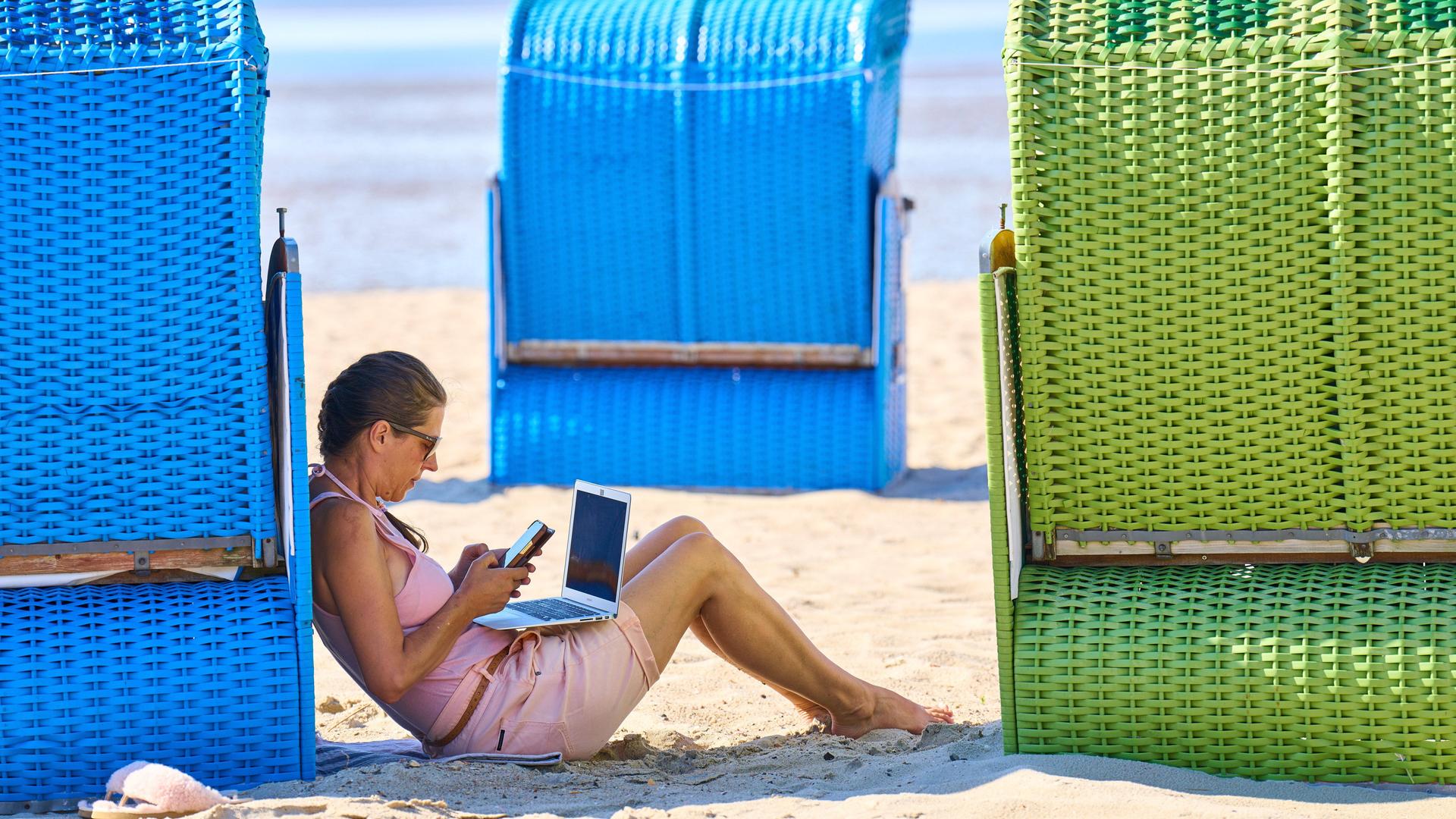 Eine Frau mit Laptop und Mobiltelefon am Strand, zwischen Strandkörben. Eine Frau mit Laptop und Mobiltelefon am Strand, zwischen Strandkörben.