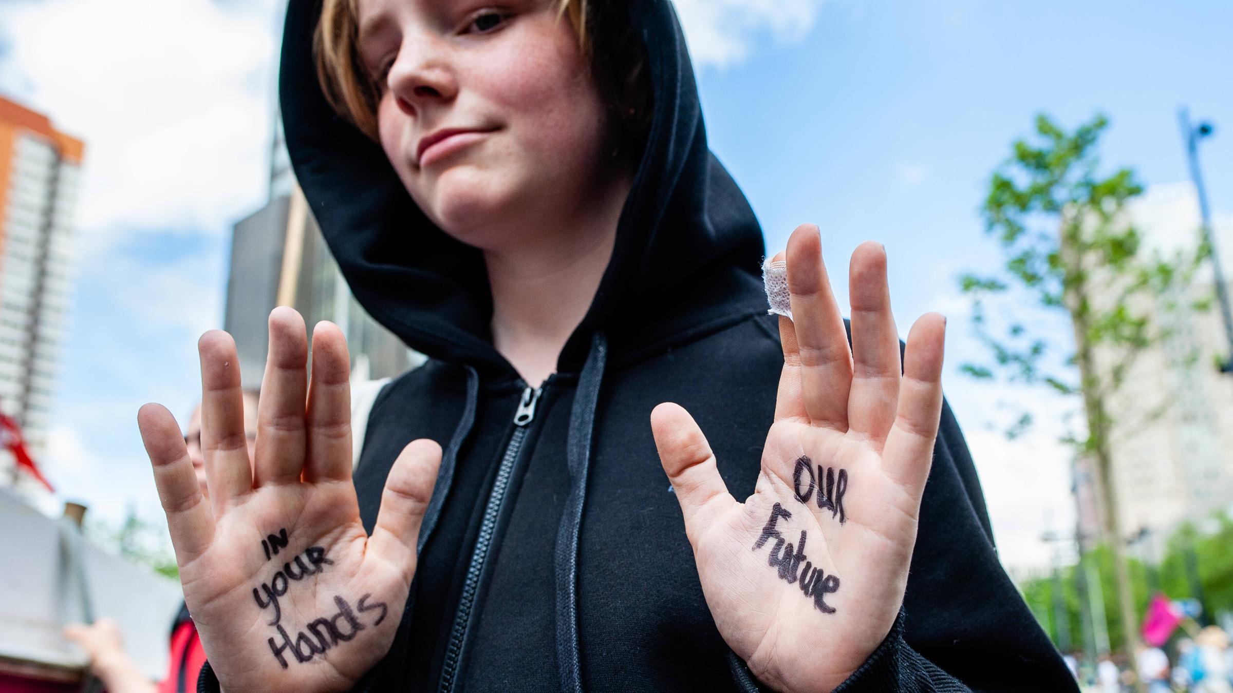 Ein junger Demonstrant der Gruppe Extinction Rebellion zeigt seine Hände, auf denen geschrieben steht: "In your Hands - Our Future", zu Deutsch: "In deinen Händen - unsere Zukunft"