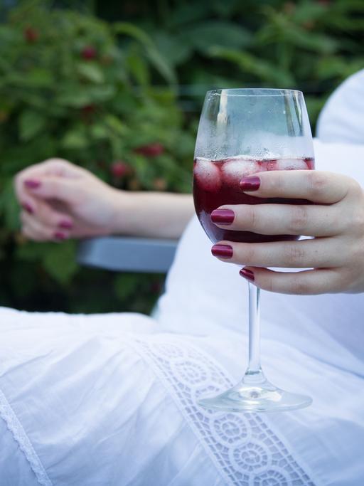 Eine schwangere Person hälft ein Weinglas in der Hand. 