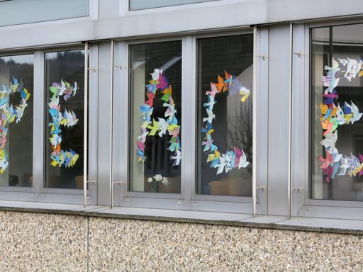 Das Wort "Peace" (deutsch: "Frieden") mit gefalteten Friedenstauben in den Fenstern einer Schule geschrieben – als Zeichen für den Frieden und gegen den Krieg in der Ukraine.