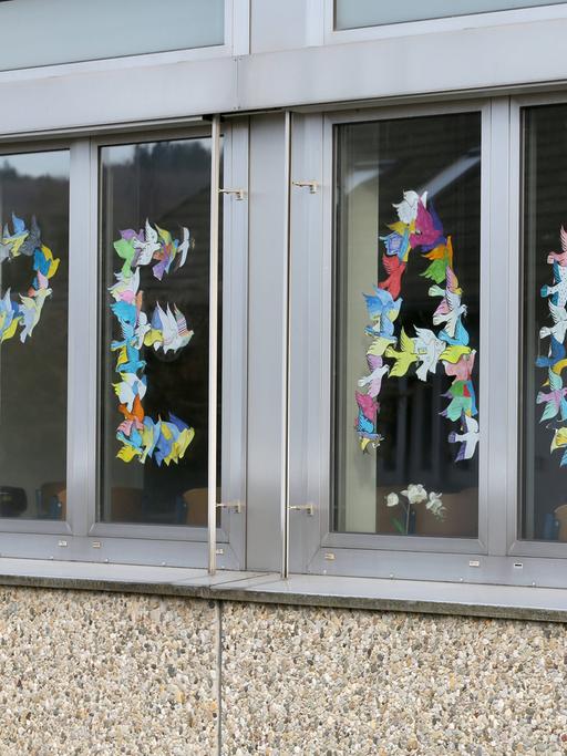 Das Wort "Peace" (deutsch: "Frieden") mit gefalteten Friedenstauben in den Fenstern einer Schule geschrieben – als Zeichen für den Frieden und gegen den Krieg in der Ukraine.
