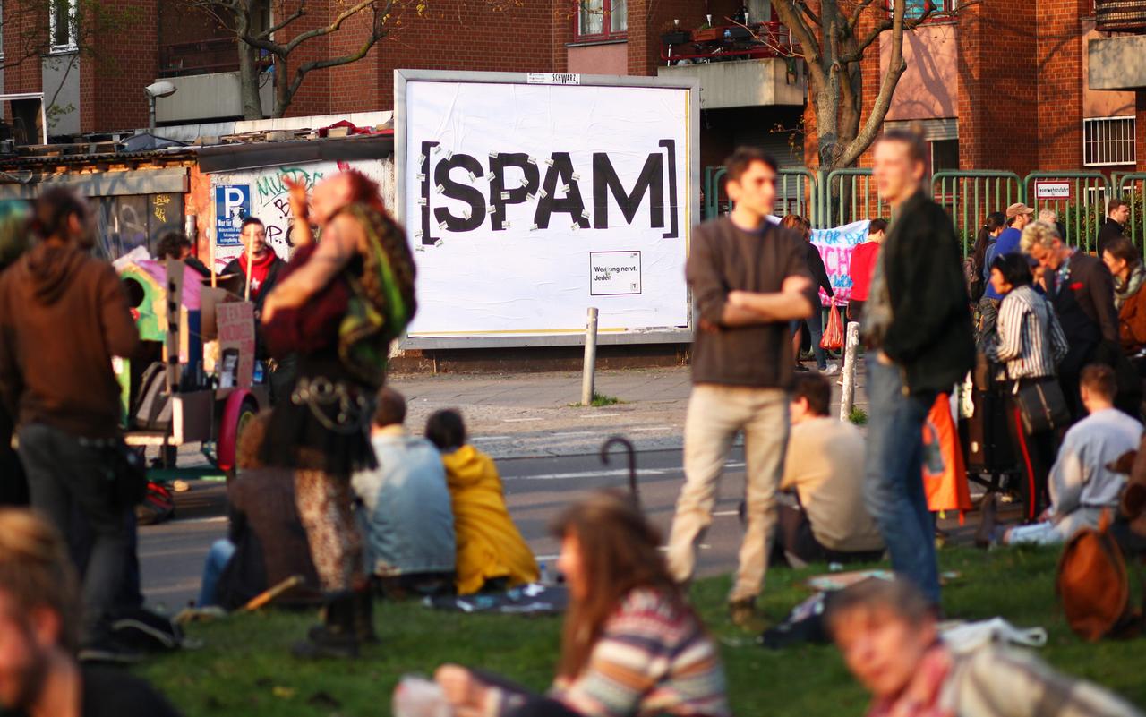 Junge Leute sitzen vor einem Plakat einer Initiative für den Volksentscheid "Berlin werbefrei". Plakate und Plakatwerbung werden darauf als "Spam" bezeichnet. Ziel der Initiative ist eine deutliche Reduzierung der kommerziellen AuÃenwerbung in der Hauptstadt und ein Verbot digitaler Werbeanlagen im öffentlichen Raum.