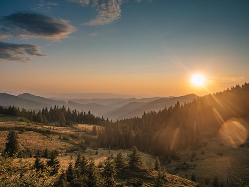 Über einem bergigen Horizont geht die Sonne mit großen Strahlen auf.