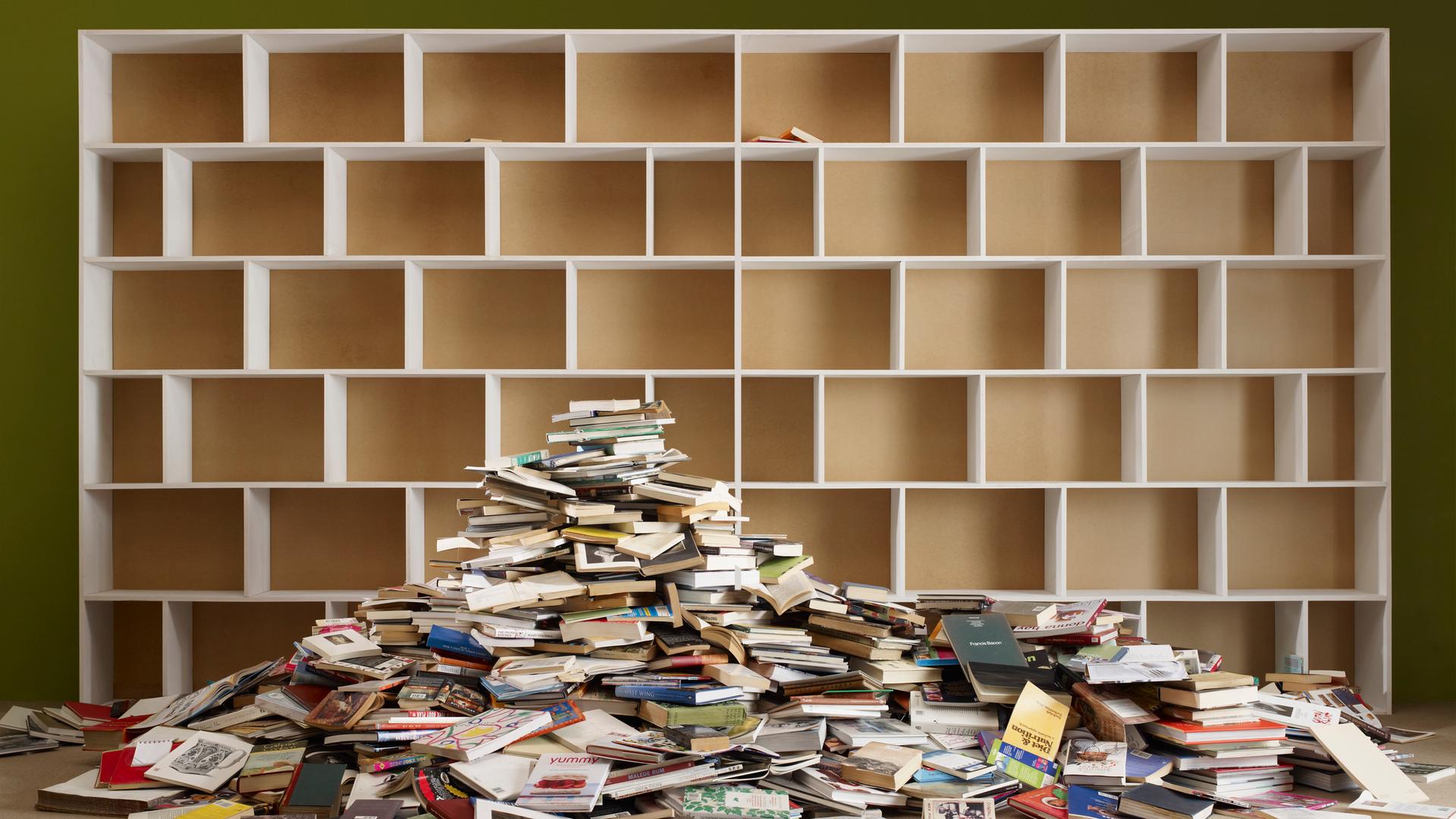 Ein leeres Regal, vor dem ein großer Bücherhaufen liegt. Ein leeres Regal, vor dem ein großer Bücherhaufen liegt.
